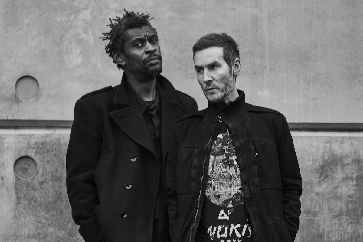 Black and white portrait of trip-hop band Massive Attack members Robert Del Naja and Grant Marshall posing together against an industrial wall